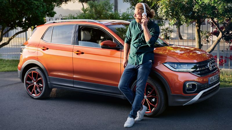 A man is leaning against the VW T-Cross and is listening to music via headphones