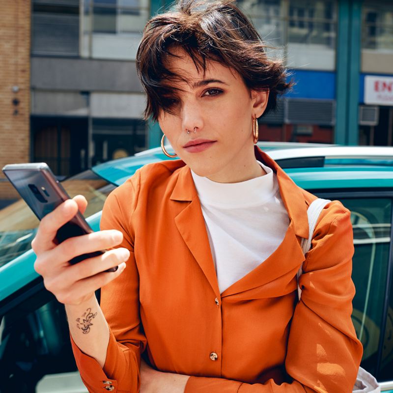 Woman holding a mobile phone standing in front of a T-Cross