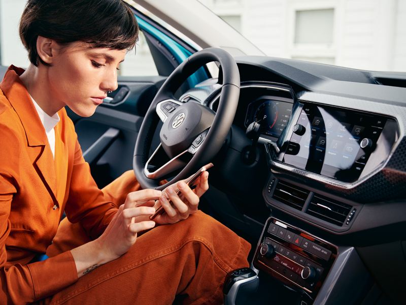Junge Frau mit Smartphone im VW T-Cross Innenraum