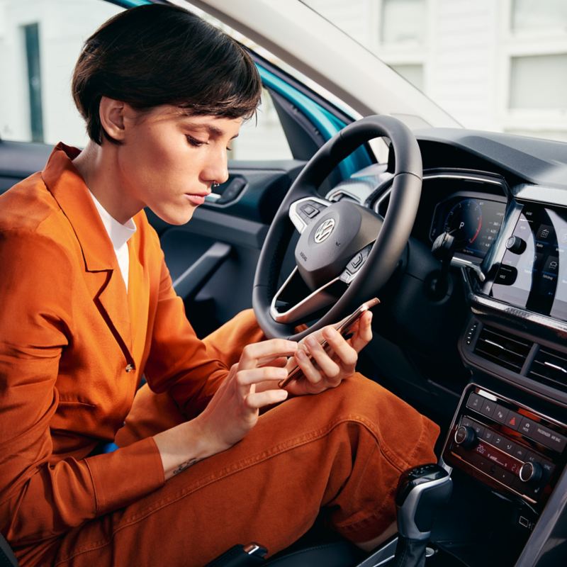 Mujer mirando un móvil sentada al volante de un coche T-Cross aparcado con la puerta abierta