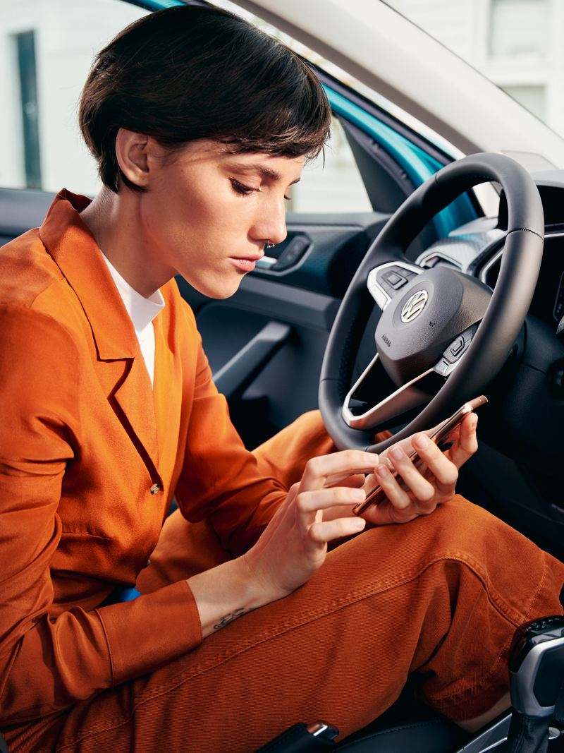 En kvinna i en VW T-Cross med mobil i handen och öppen dörr.