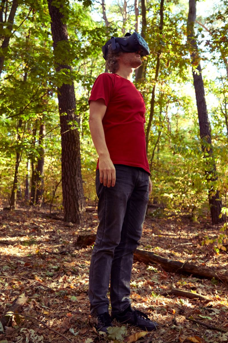 Leo is standing in nature with VR glasses over his eyes.