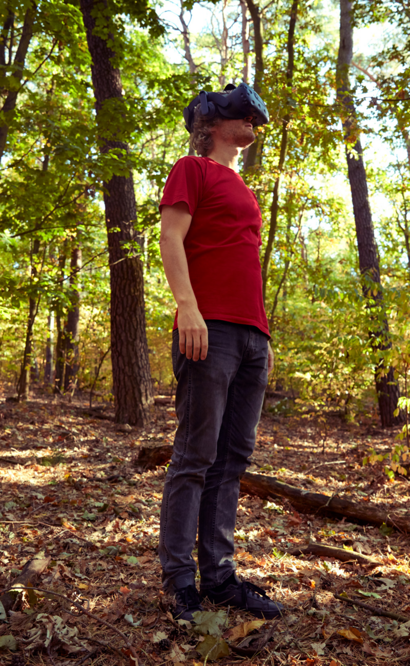 Leo is standing in nature with VR glasses over his eyes.