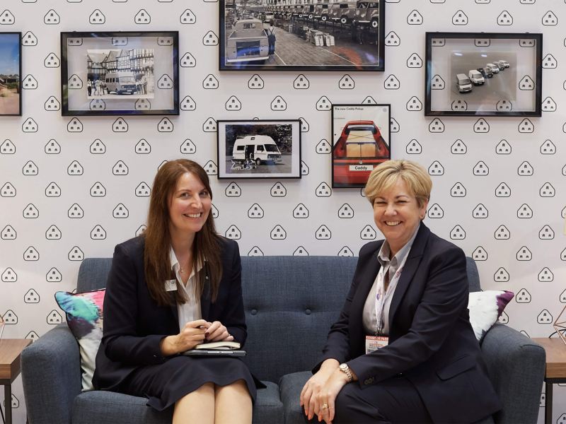 Two women smiling, sitting on a sofa inside the VW Commercial Vehicle show living room 