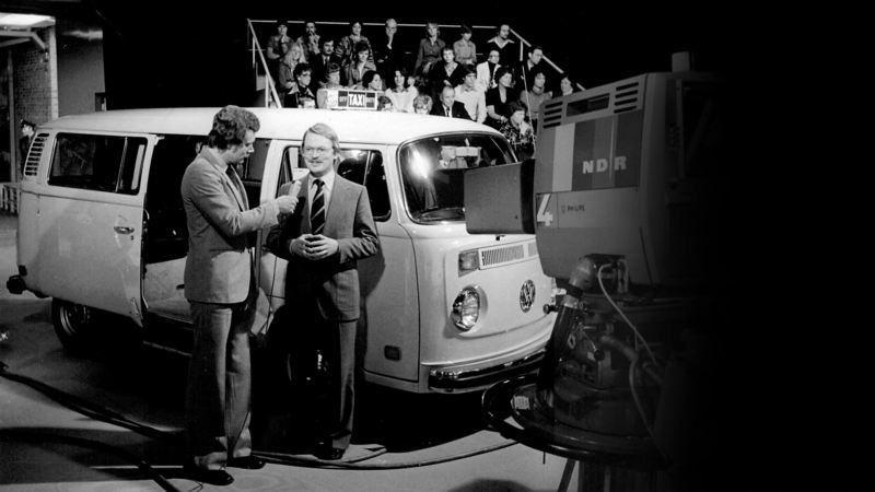 Black and white photograph of E-campervan and Adolf Kalberlah being interviewed for TV show