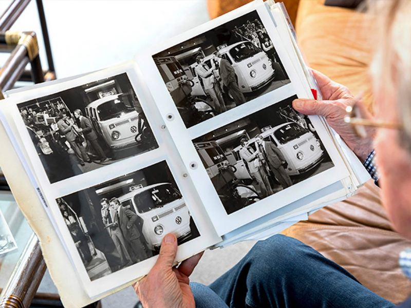 Person looking at old black and white photographs of a camper van being charged