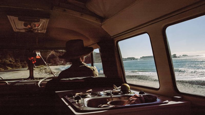 Woman sitting in camper van looking out to the beach