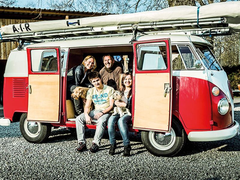 Red and white camper van with family and dogs sitting inside
