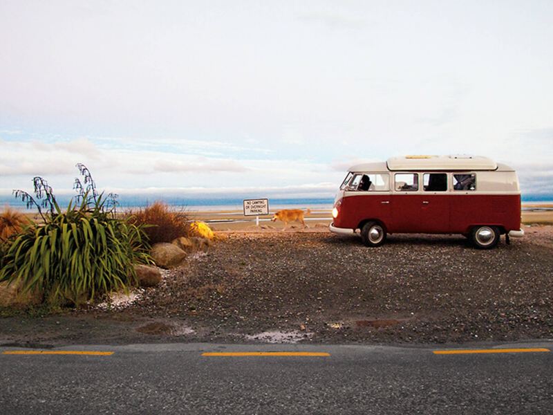 Red and white camper van on the beach with dog