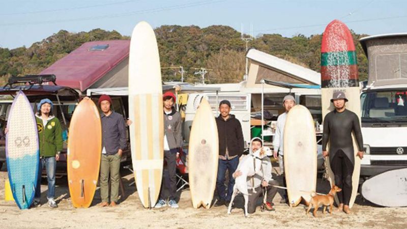 Men on beach with surfboards standing in front of camper vans