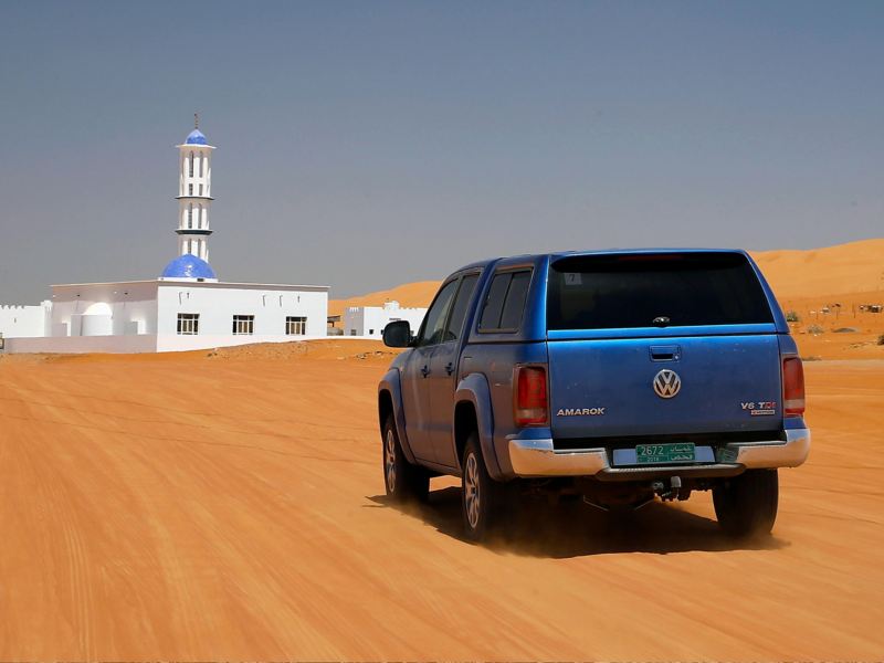 Blue Amarok drive through desert towards building
