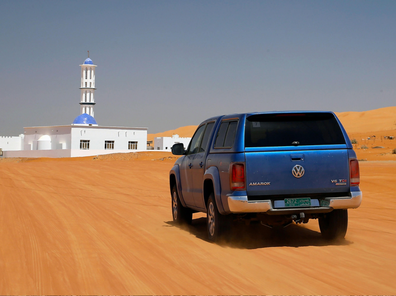 Blue Amarok drive through desert towards building