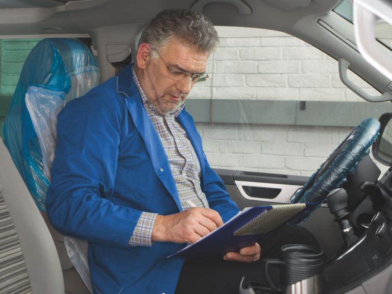 Ein Mann sitzt in einem Fahrzeug und füllt einen Prüfbogen aus.