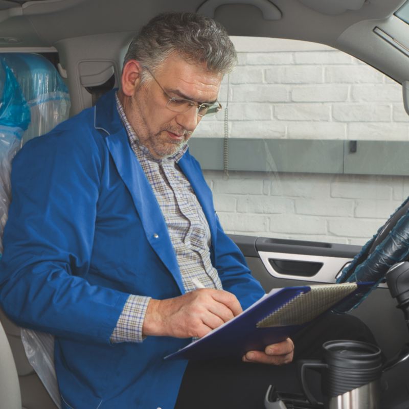 Ein Mann sitzt in einem Fahrzeug und füllt einen Prüfbogen aus.
