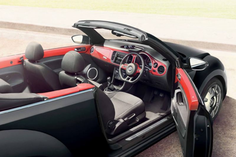 Interior shot of a red Volkswagen Beetle Cabriolet, next to the beach with the roof down and the drivers door open.