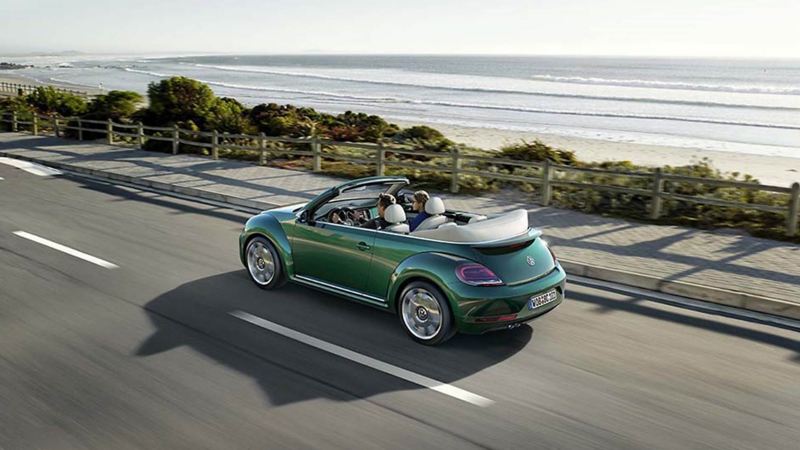 A couple driving in a green VW Beetle Cabriolet