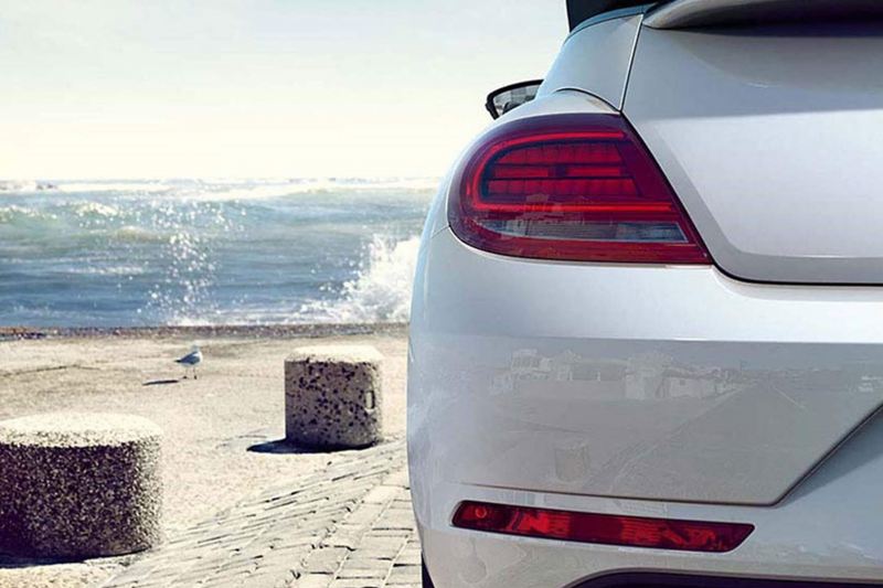 Rear shot of a white Volkswagen Beetle with the sea in the background.