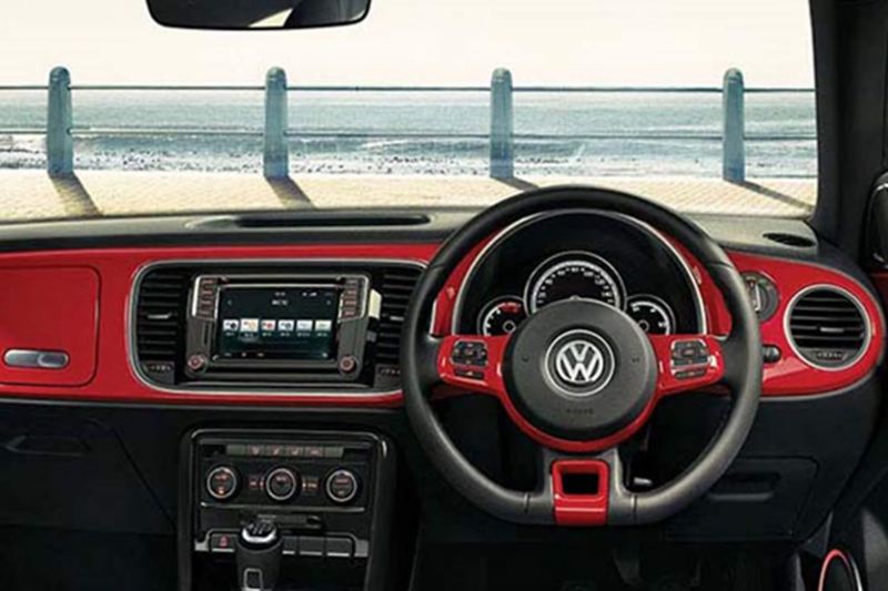Interior dashboard and steering wheel shot of a Volkswagen Beetle Cabriolet, on a promenade with the sea in front.