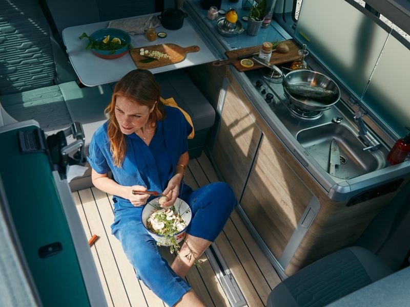 Kvinna sitter i köket i en VW California husbil