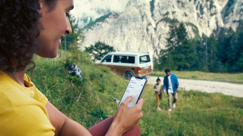 Une personne tenant un smartphone à la main avec la télécommande California est assise sur une colline.