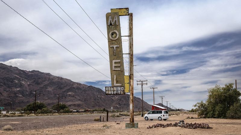 Der Volkswagen Nutzfahrzeuge California hält hinter einem großen „Motel“-Schild an einem kalifornischen Highway.