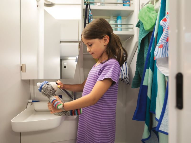 Une fillette est devant le lavabo du Grand California, elle lave les dents de son ours en peluche.