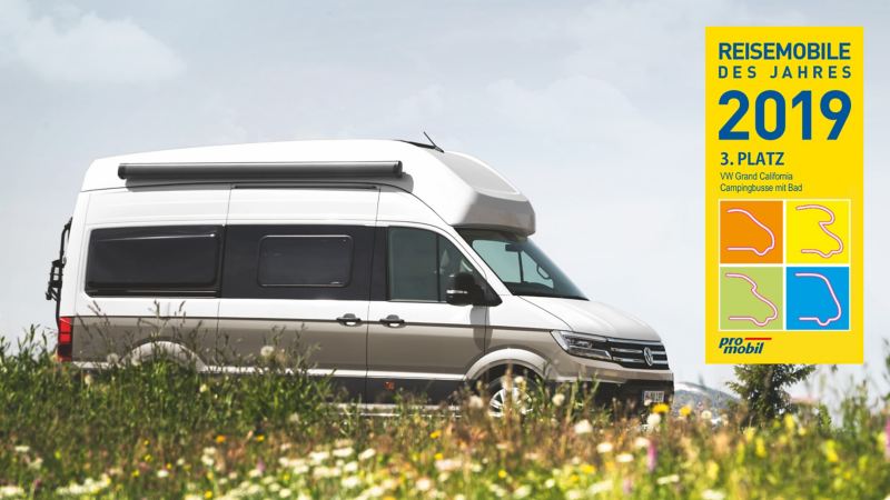 Le Grand California roule à travers un champ de fleurs sauvages. Sur la photo, on voit le logo du camping-car de l'année 2019 avec la mention « 1ère place ». 