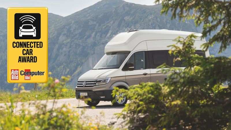 Le Grand California roule dans un paysage de montagnes impressionnant. Sur la photo, on remarque le logo du prix Connected Car Award 2019. 