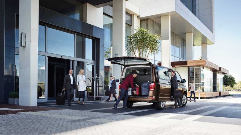 En brun VW Caravelle minibuss packas med resväskor utanför ett hotell