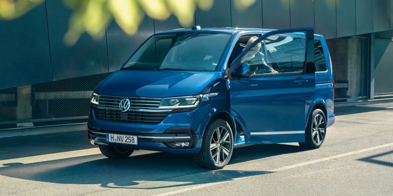 Ein VW Caravelle 6.1 schräg von der Seite. Ein Mann steigt in das Fahrzeug ein.