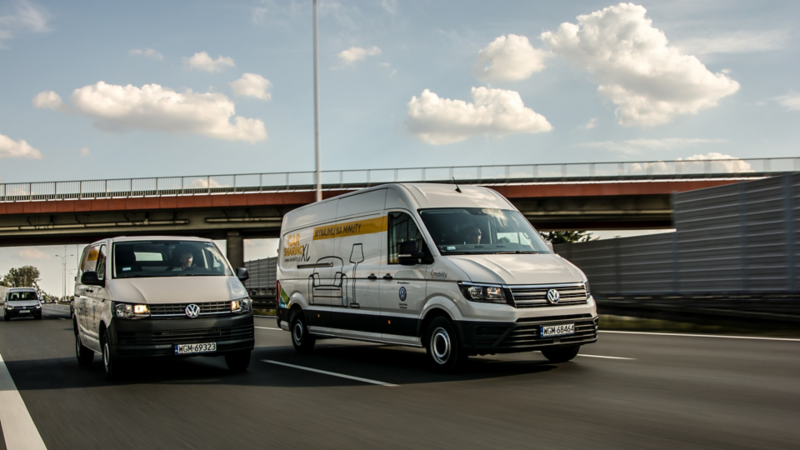 Transporter i Crafter w okleinie o carsharingu jadą po drodze, w tle most