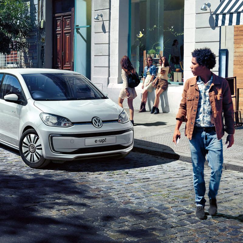 A white Volkswagen up! in a cobbled shopping street, pedestrians shopping.