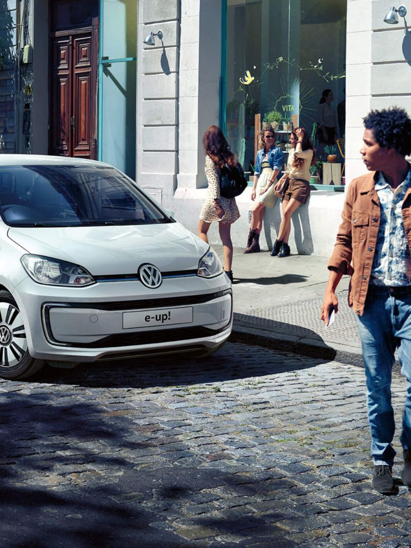 A white Volkswagen up! in a cobbled shopping street, pedestrians shopping.