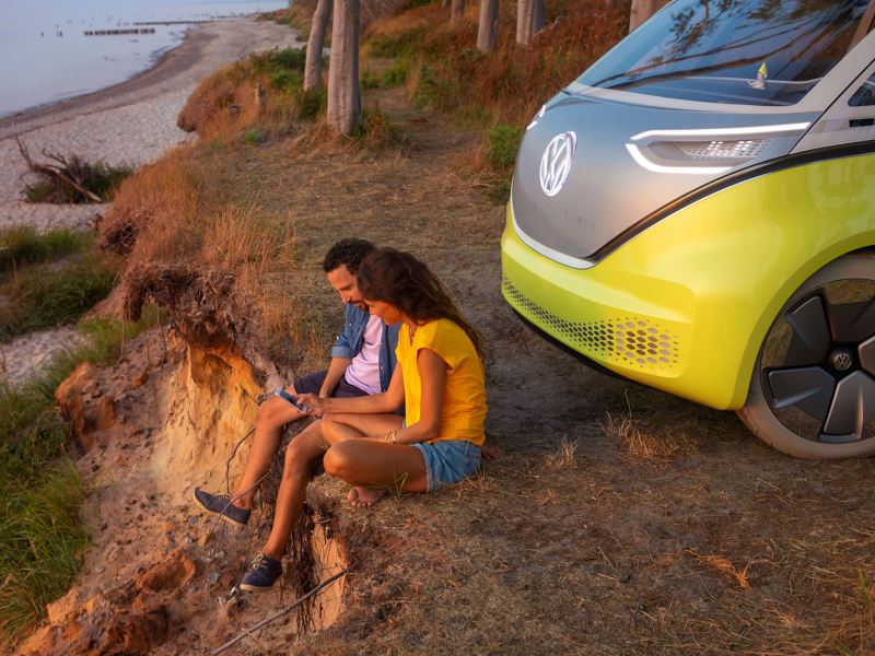 A couple sitting in nature by their parked Electric car