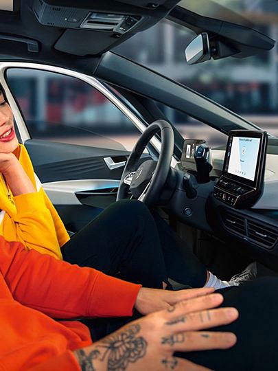 Žmonės „ID.3“ automobilyje; moteris su išmaniuoju telefonu
