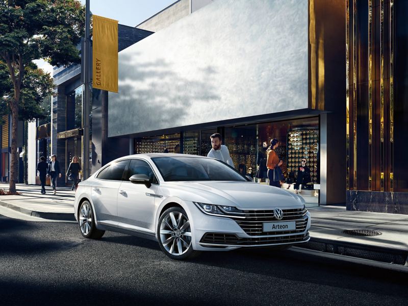 A white Volkswagen Arteon parked on a city street outside of shops, the owner getting in.