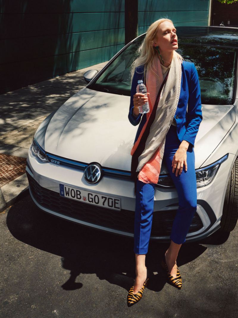 VW Golf GTE blanche stationnée dans une rue avec une femme assise sur le capot