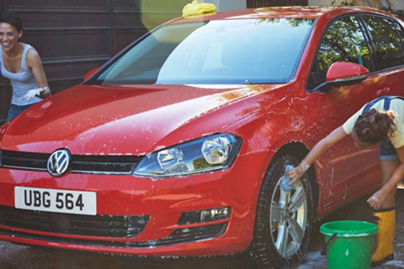 A red Volkswagen Golf, being washed by two friends.