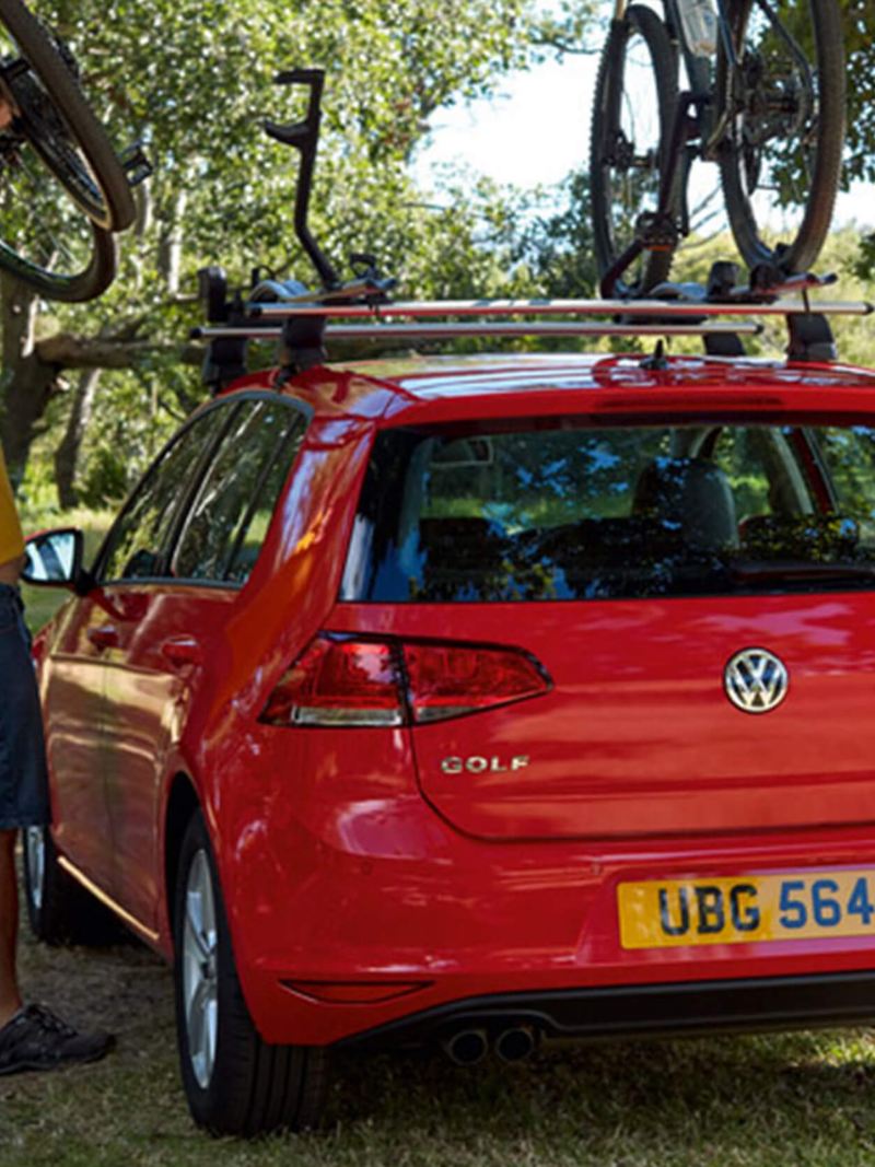 A man hitching his bike to the roof rake of a Volkswagen Golf, surrounded by woodland