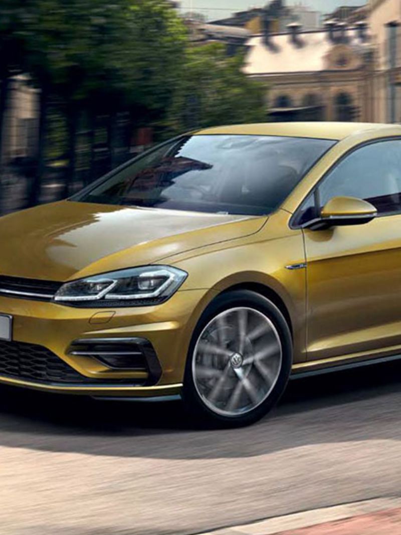 A gold Volkswagen Golf R-Line, driving through an old city.
