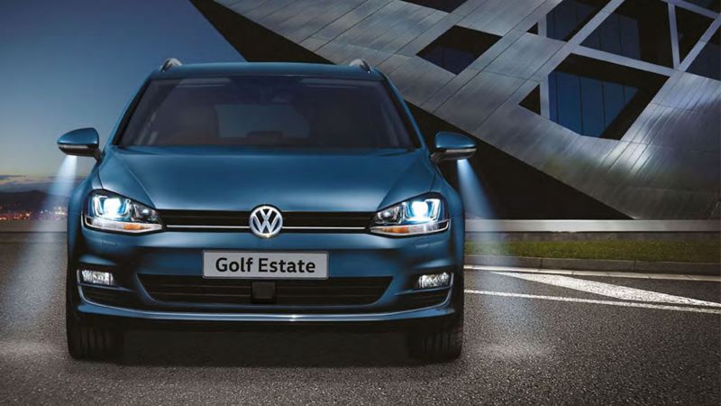 Front headlight shot of a dark blue Volkswagen Golf Estate., at night. Wing mirror lights on.
