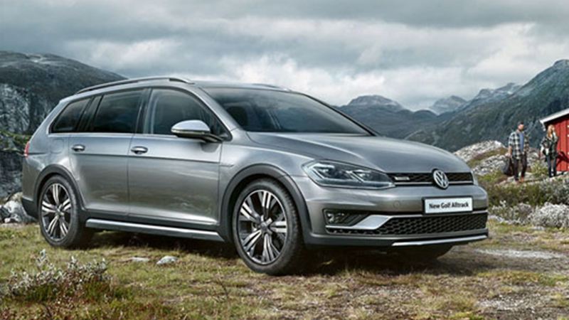 A silver Volkswagen Golf Estate, next to a cabin, in the mountains.