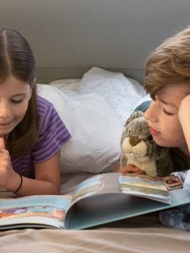 En lille dreng og hans søster ligger i køjesengen i Grand California og læser en bog sammen.