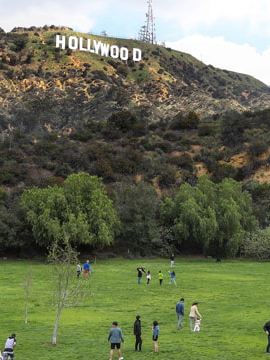 Menschen stehen auf einer grünen Wiese, im Hintergrund der Schriftzug des Hollywood Sign.