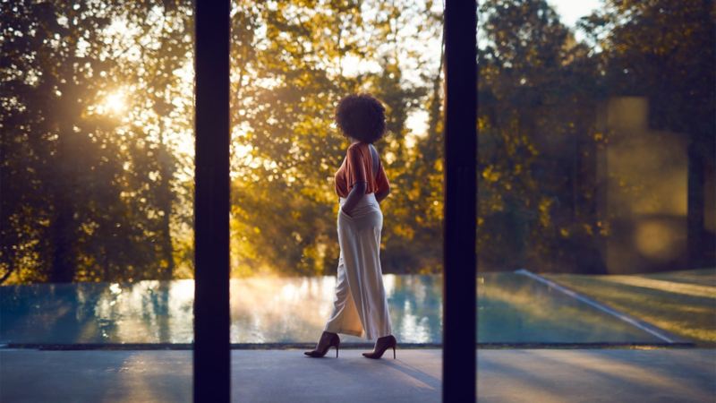 A woman is walking next to a pool nd looks into the sky, View through the window