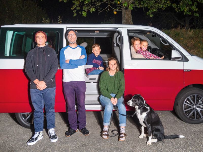 Una famiglia di sei persone sta davanti a un Multivan parcheggiato.