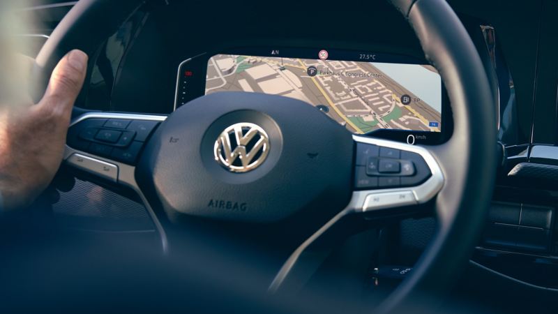 Una mano guida un volante, sul display è possibile vedere la mappa di un sistema di navigazione.