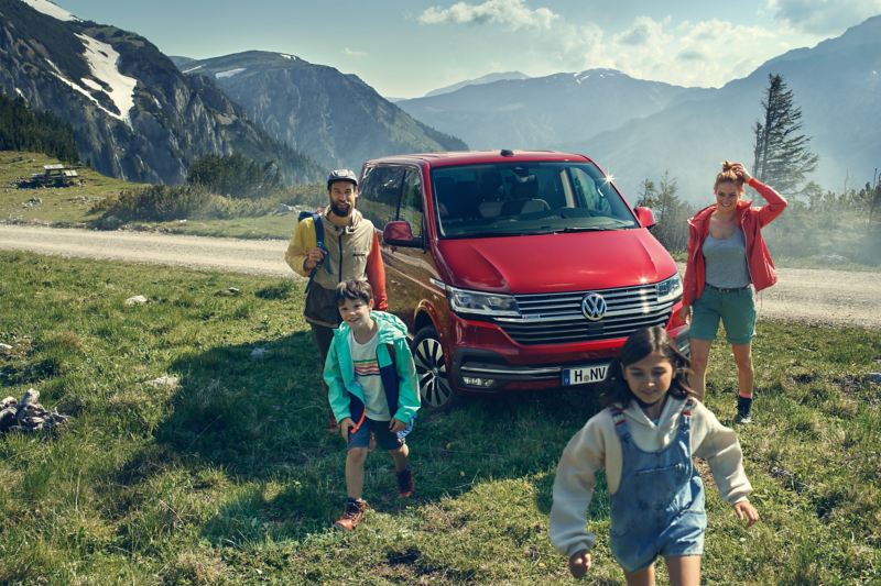 En begagnad röd VW Multivan minibuss omgiven av en barnfamilj uppe i bergen.