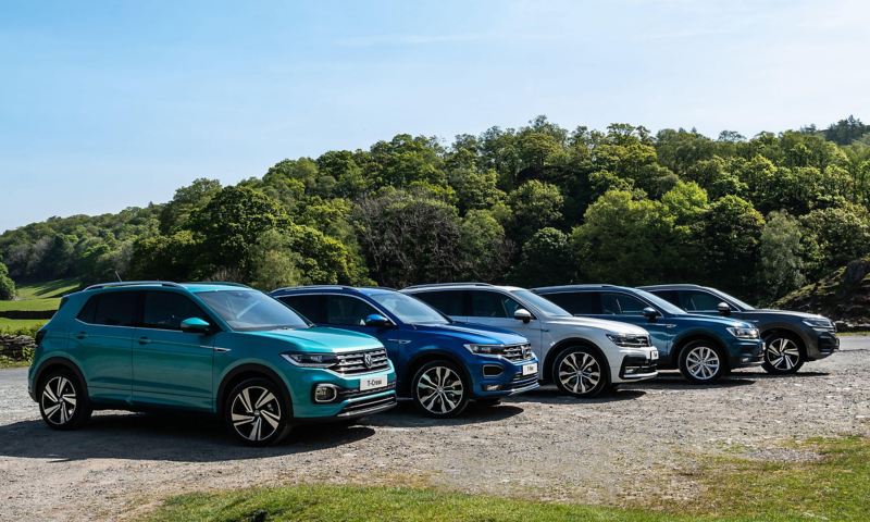 A Volkswagen T-Roc, T-Cross, Tiguan, Tiguan Allspace and Touareg parking in the mountains in front of a lake.