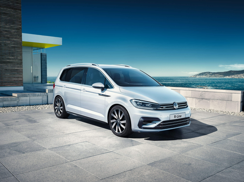 A white Volkswagen Touran outside a building with a bay and white cliffs in the background.